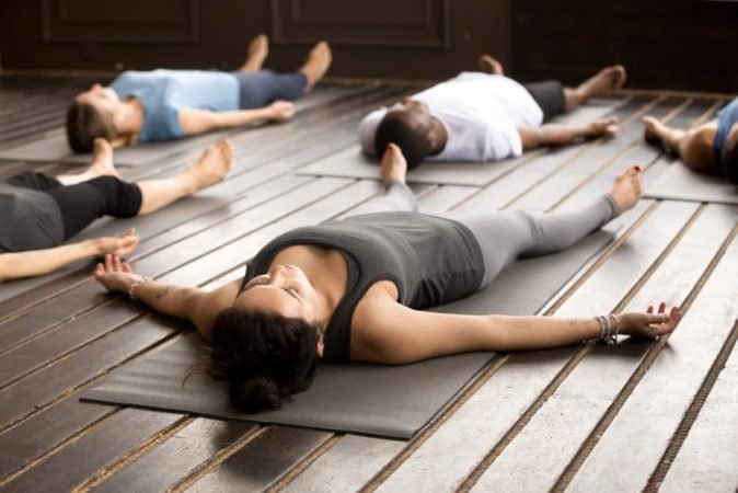 Group of young afro american and caucasian sporty people practicing yoga lesson lying in Dead Body pose, Savasana exercise, working out, resting after practice, indoor close up, studio